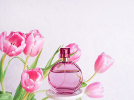 bottle of perfume with flowers pink tulips on white concrete background